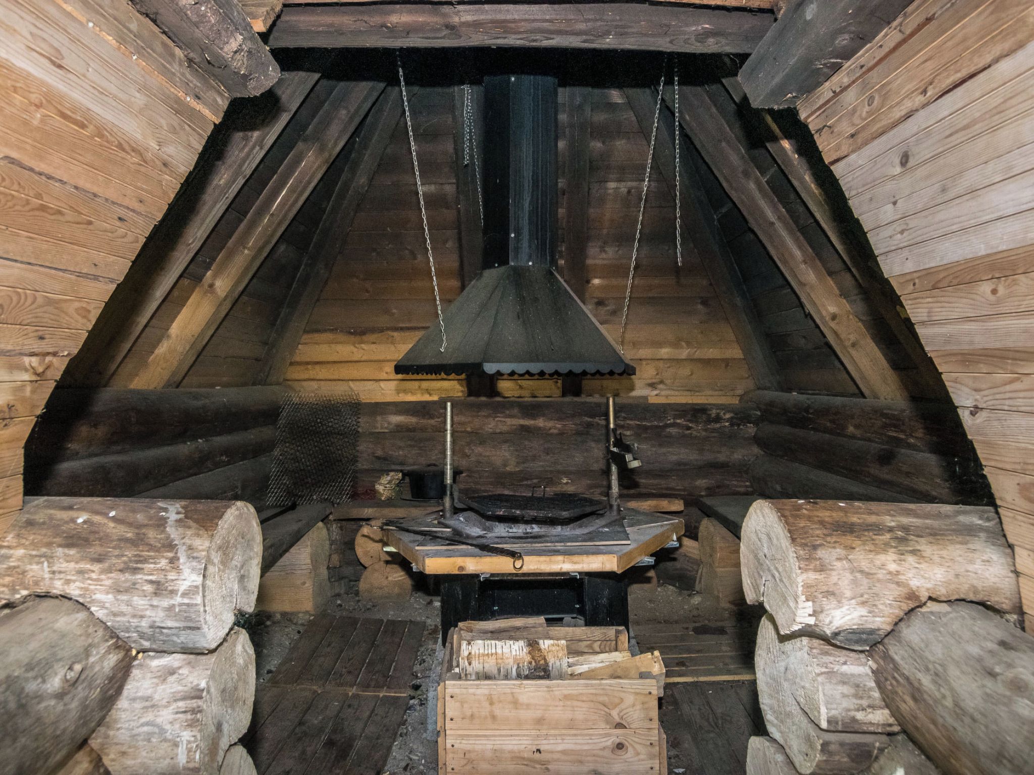 A log cabin interior with a central fireplace, wooden logs, and a metal grate.