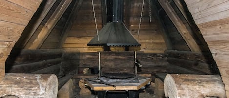A log cabin interior with a central fireplace, wooden logs, and a metal grate.