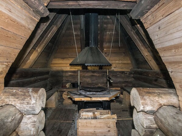 A log cabin interior with a central fireplace, wooden logs, and a metal grate.