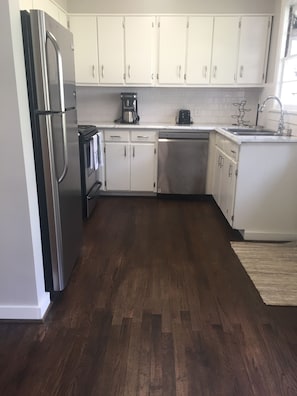 Una cocina con armarios blancos, electrodomésticos de acero inoxidable y piso de madera.