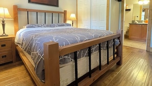 A bedroom with a wooden bed, two bedside tables with lamps, a framed picture on the wall, and a door leading to a bathroom. - LUXURY CONDO GROUND FLOOR, STEPS TO POOL, 2 BEDROOMS, 1 BATH, SLEEPS 5 (Osoyoos)