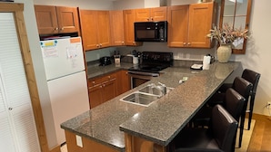 A kitchen with wooden cabinets, a granite countertop, a stainless steel sink, a microwave, a stove, and a vase with dried plants. - LUXURY CONDO GROUND FLOOR, STEPS TO POOL, 2 BEDROOMS, 1 BATH, SLEEPS 5 (Osoyoos)