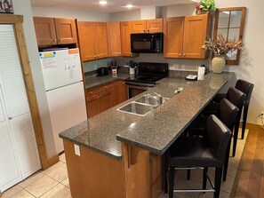 A kitchen with wooden cabinets, a granite countertop, a stainless steel sink, a microwave, a stove, and a vase with dried plants. - LUXURY CONDO GROUND FLOOR, STEPS TO POOL, 2 BEDROOMS, 1 BATH, SLEEPS 5 (Osoyoos)