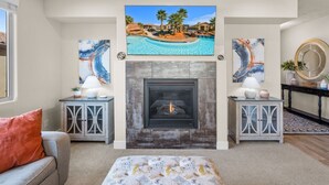 Una sala de estar con chimenea, dos mesitas de noche con lámparas, un sofá y un televisor grande sobre la chimenea.