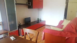 Een functionele woonruimte met een kitchenette, een eethoek met tafel en stoelen, en een zithoek met een bank.