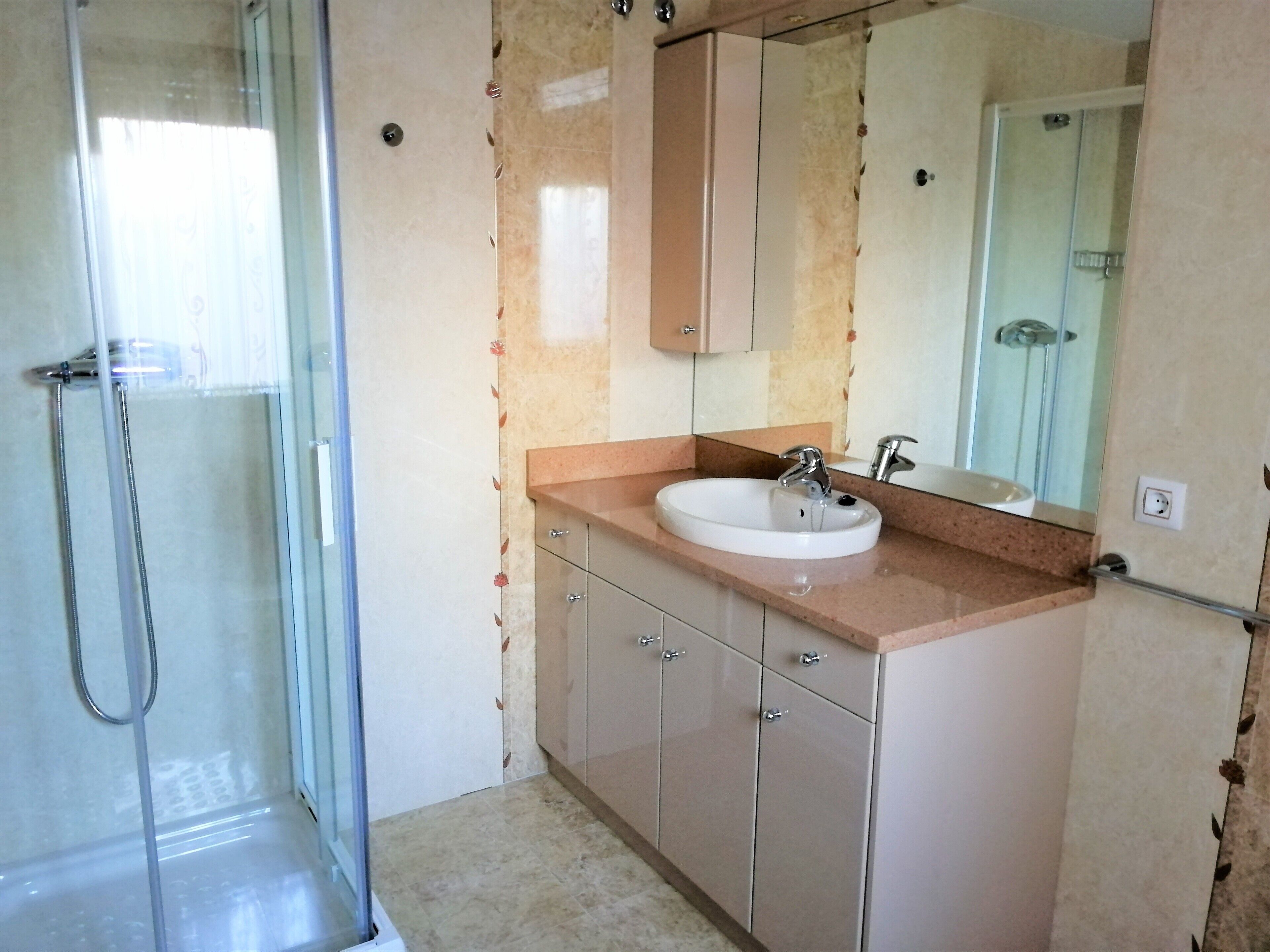 Ein Badezimmer mit Duschkabine aus Glas, einem Waschbecken mit Spiegel und beige farbenen Schränken.