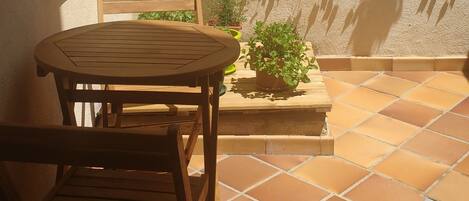 A patio with a round wooden table and chairs, a white lattice wall with climbing plants, and a tiled floor.