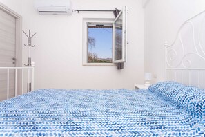 A bedroom with a bed, a window, a coat rack, and a radiator.