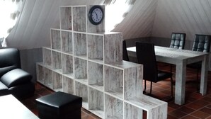 A modern, loft-style room with a high ceiling, a dining table with chairs, a black sofa, and a white shelving unit. - Lovingly furnished apartment is looking forward to young and old guests.  (Friedeburg)