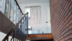 A staircase with metal railings and wooden steps leading to a room with a white wall and a window with curtains. - Lovingly furnished apartment is looking forward to young and old guests.  (Friedeburg)