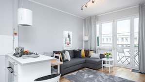 Un apartamento moderno con cocina, un sofá gris, zona de comedor y grandes ventanales con vistas a la ciudad.