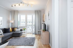 A modern living room with a grey sectional sofa, a small white table with a vase of flowers, a grey rug, and a wooden cabinet.