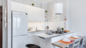 Una cocina moderna con armarios blancos, un refrigerador empotrado, una isla central con asientos y un comedor con mesa y sillas.