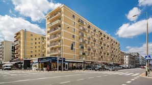 Un hotel de varios pisos con balcones, un paso de peatones y diversas tiendas.