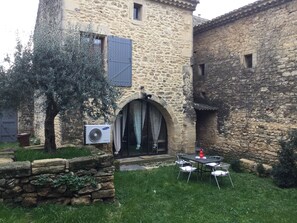 A stone building with a courtyard, a table and chairs, and a tree.