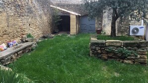 A rustic courtyard with stone walls, a grassy area, and a wooden bench. - Beautiful stone house in the village of Vers Pont du Gard (Vers-Pont-du-Gard)