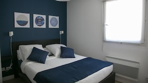 Ein ordentlich bezogenes Bett mit weißer und blauer Bettwäsche, ein dunkles Kopfteil und eine Wand mit drei gerahmten Kunstwerken.