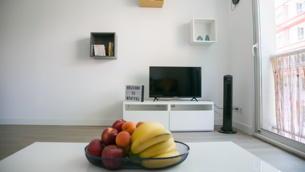 Ein modernes Wohnzimmer mit Fernseher, Obstschale, Kaktee und einer Willkommensschild.