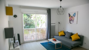 Ein modernes Wohnzimmer mit grauem Sofa, blauem Teppich und einer Obstschale auf einem weißen Couchtisch.
