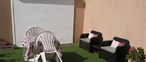 An outdoor seating area with two white chairs and two black sofas, a table with a pink tablecloth, and a potted plant.