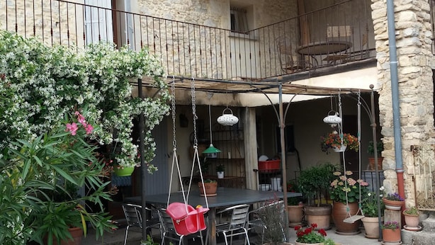 Un edificio in pietra con un balcone, posti a sedere all'aperto e piante in vaso.