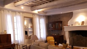 Un soggiorno con pianoforte, divano e poltrone. È presente un caminetto e uno specchio a parete.