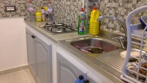 A kitchen with a gas stove, sink, and various cleaning supplies. - A charming F1 studio (Sahloul)