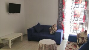 A living room with a blue sofa, a white coffee table, and a patterned tablecloth. - A charming F1 studio (Sahloul)