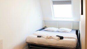 Een kleine, lichte kamer met een enkel bed, een raam en een hangende lamp.