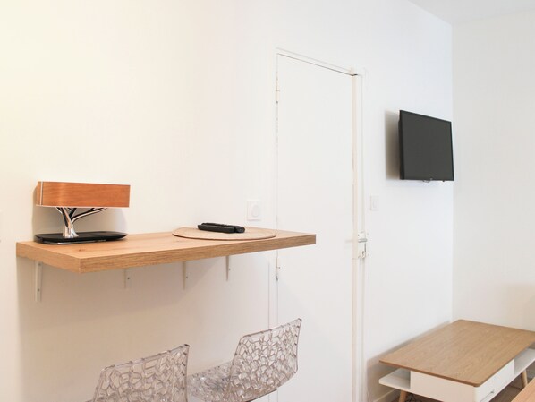 A minimalist room with a wooden desk, a chair, a mounted TV, and a lamp on a floating shelf.
