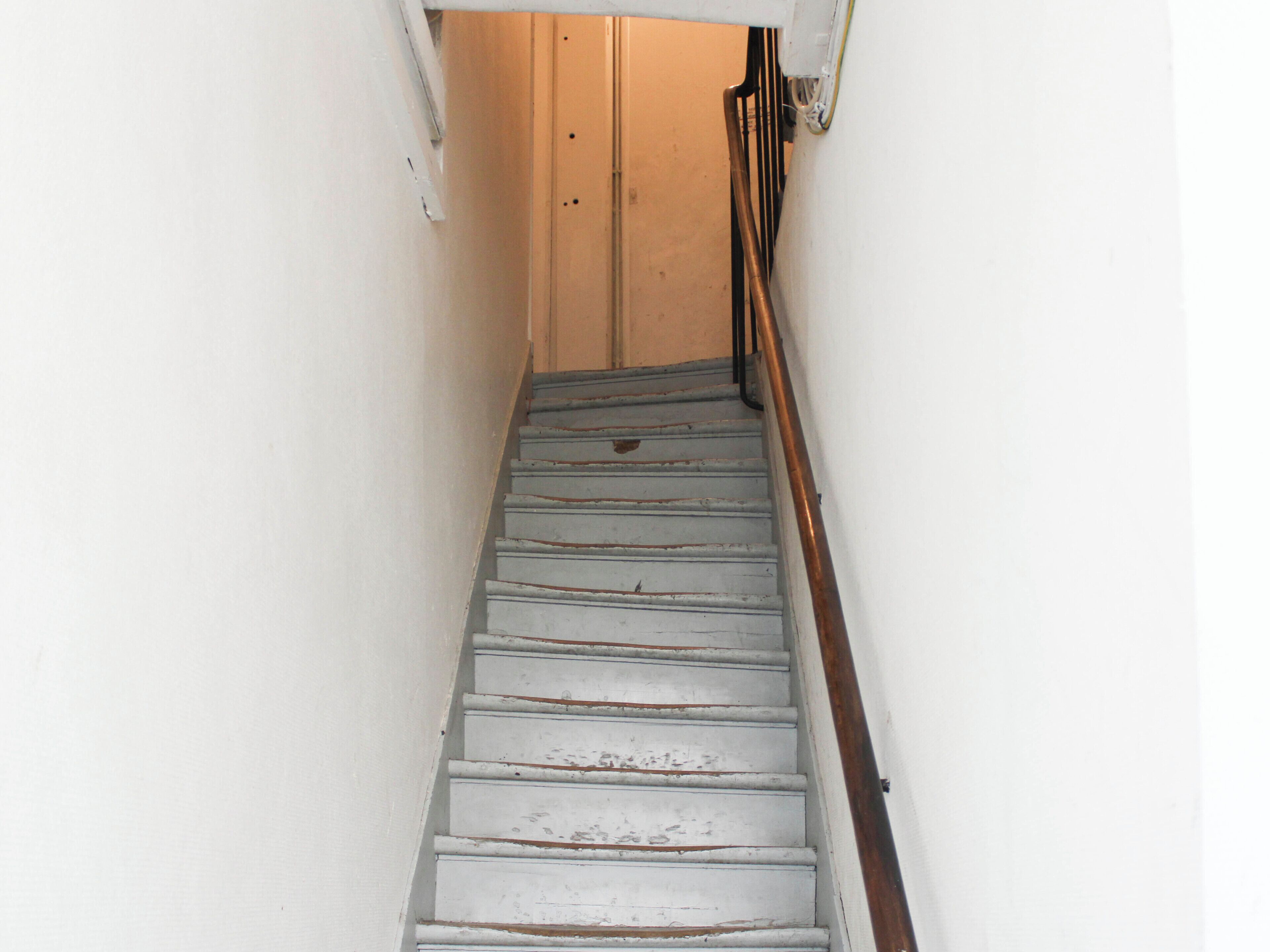 Un escalier étroit avec des marches peintes en blanc et une main courante en bois.