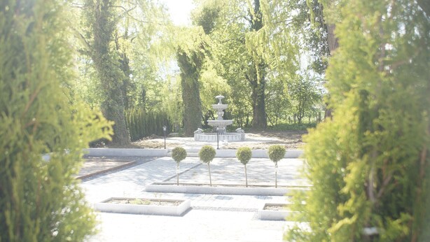 Un jardín con una fuente central, rodeado de setos y árboles bien cuidados.