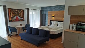 Una habitación de hotel moderna con un sofá azul, una cama con ropa blanca, una mesita y un rincón americano.