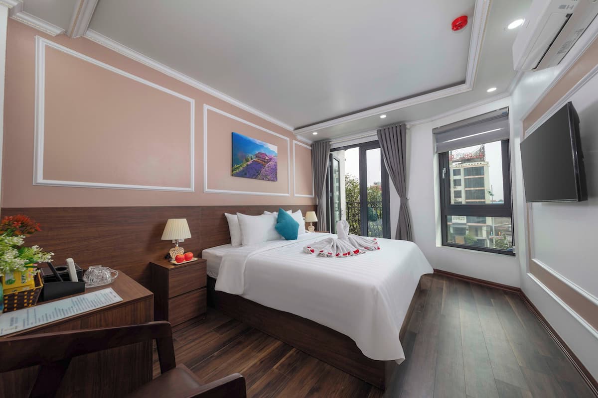 A hotel room with a large bed, a desk with a lamp, a TV, and a window with curtains.