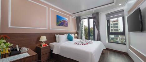 A hotel room with a large bed, a desk with a lamp, a TV, and a window with curtains.