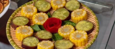 A plate of sliced vegetables including corn, cucumbers, and eggplants, arranged on a decorative plate with a red rose centerpiece.