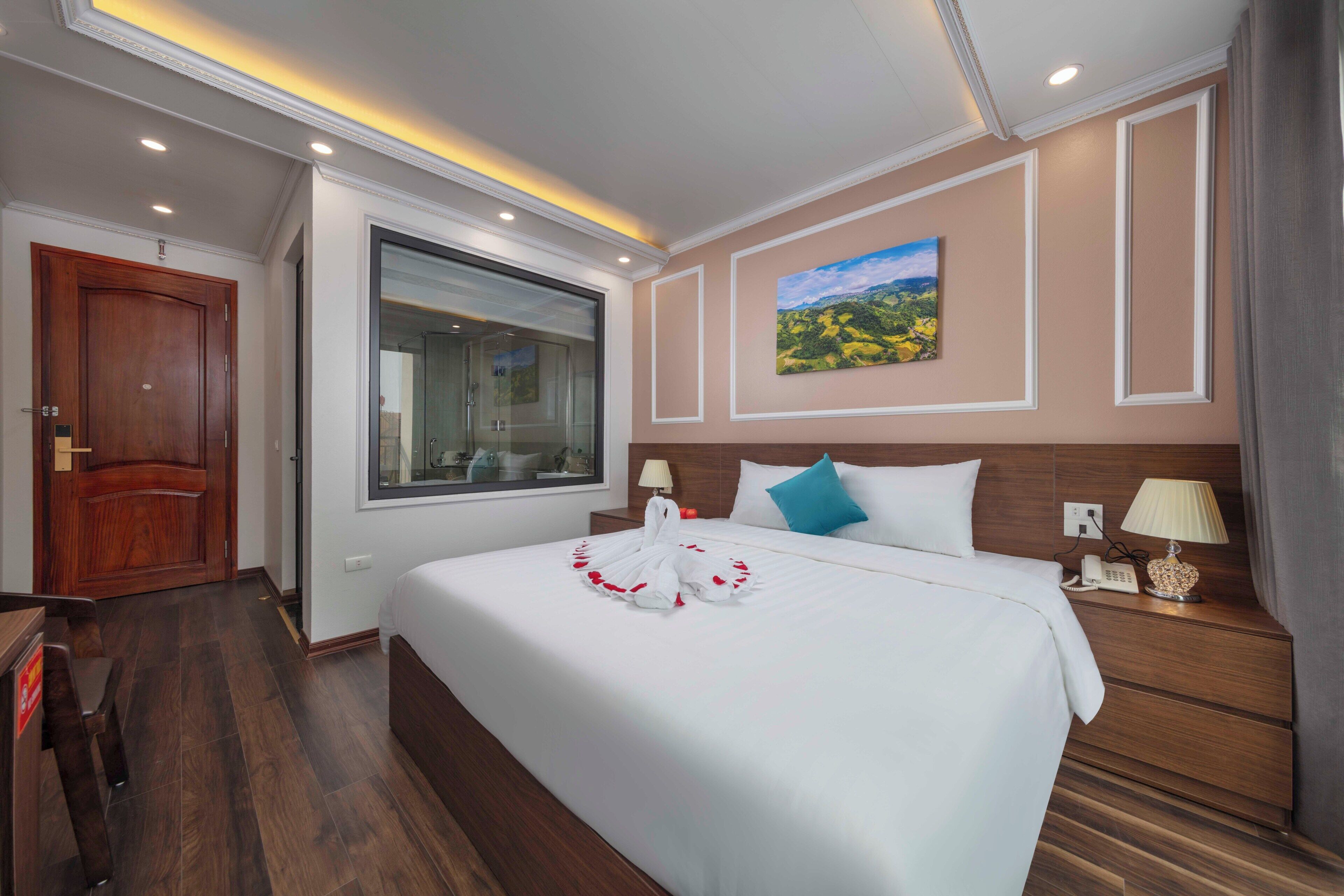 A hotel room with a large bed, wooden headboard, a window, and a painting on the wall.