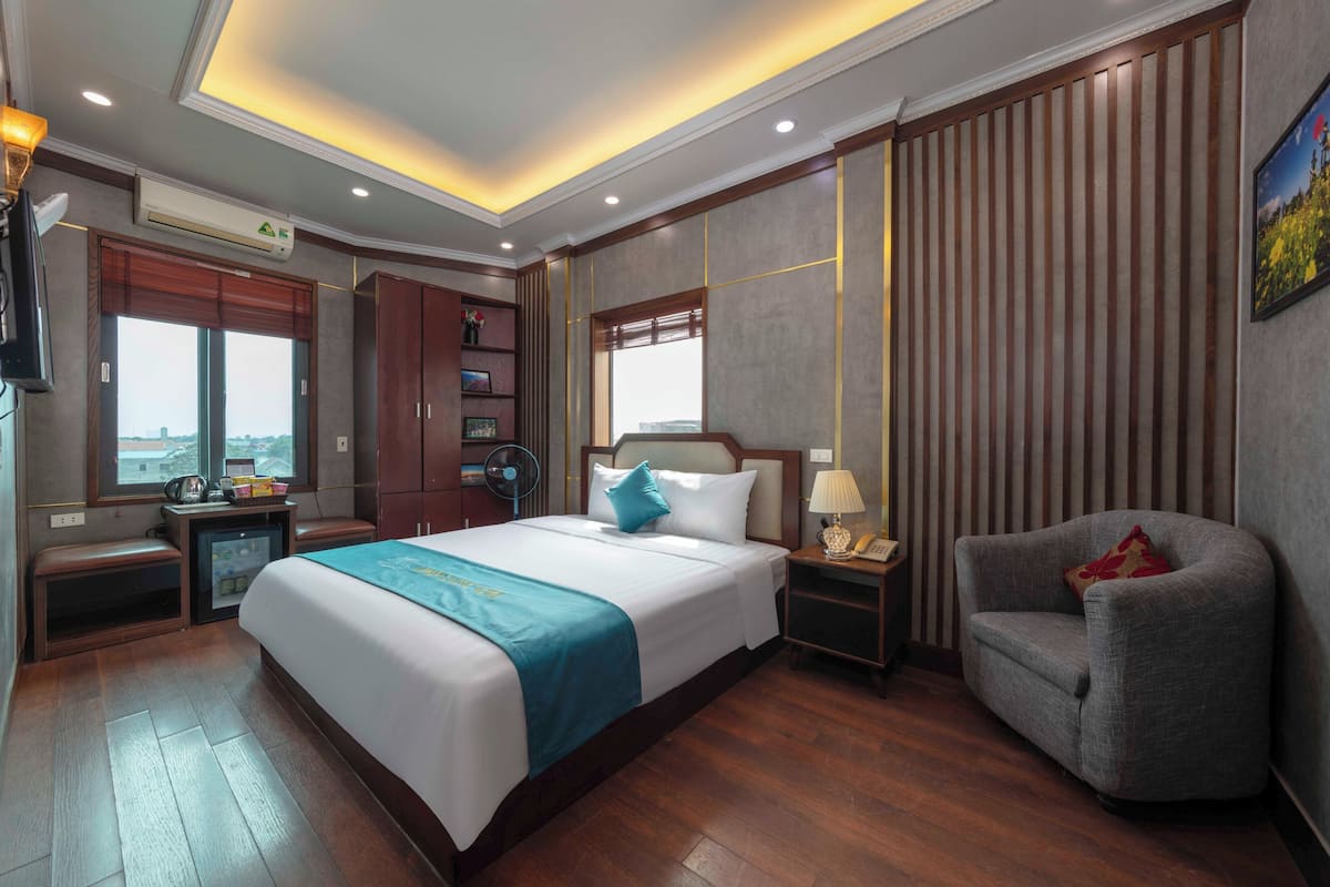 A hotel room with a large bed, a sofa, a desk, and a window with a city view.