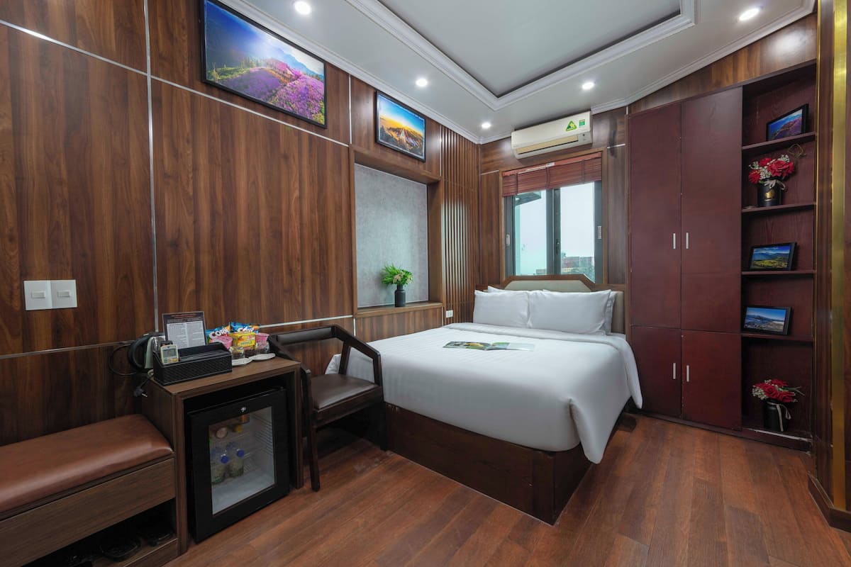 A hotel room with a bed, a desk, a refrigerator, a bench, a wardrobe, and a window with a view.