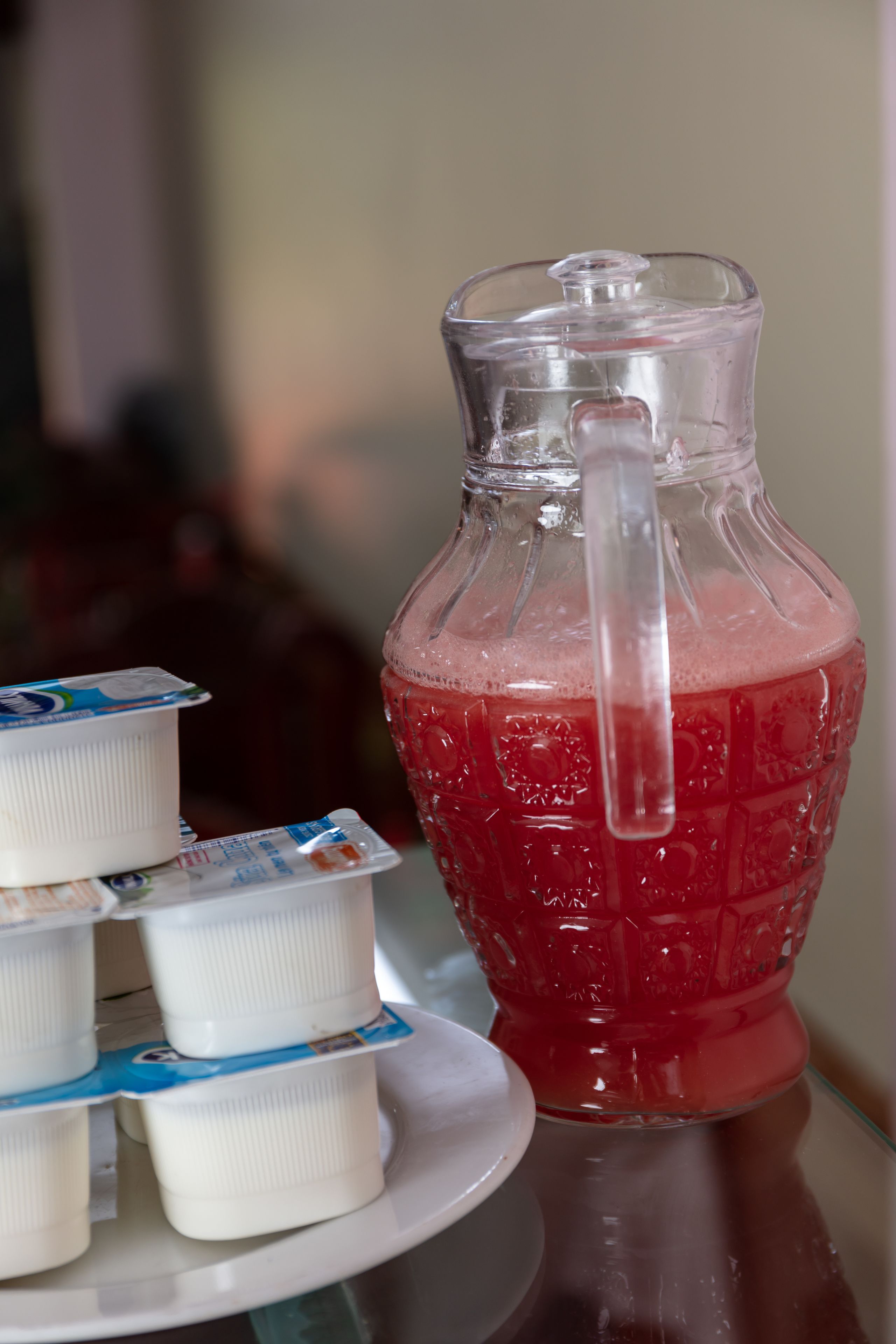 Une carafe en verre contenant une boisson rouge et une assiette blanche avec des pots de yaourt.