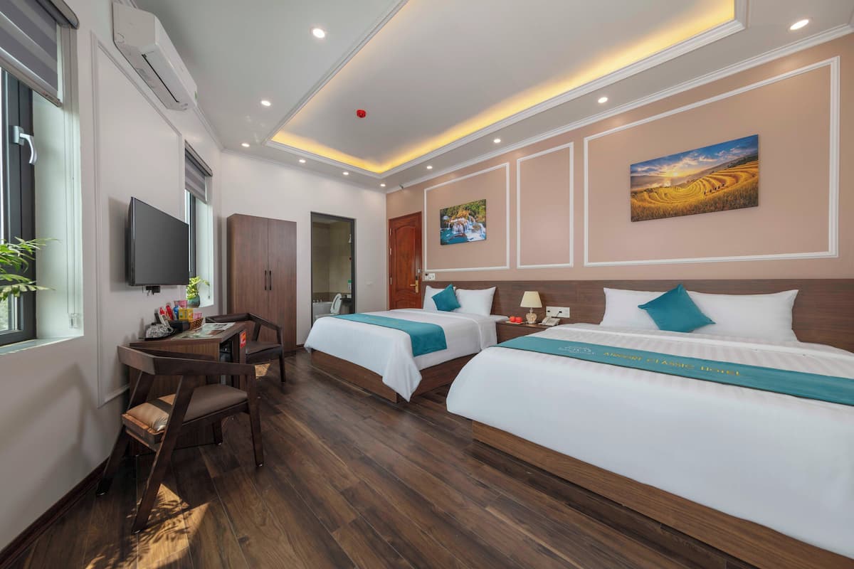 A hotel room with two beds, a desk, a TV, and artwork on the walls.