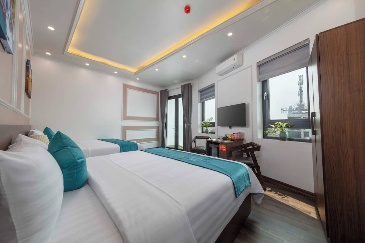 A hotel room with two beds, a desk, a TV, and a window with a view of a building.