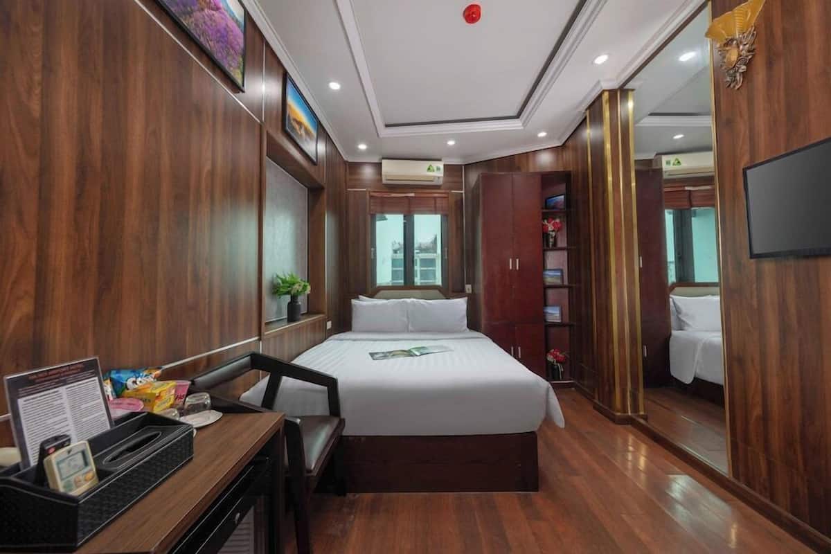 A hotel room with a bed, desk, chair, and a mirror.