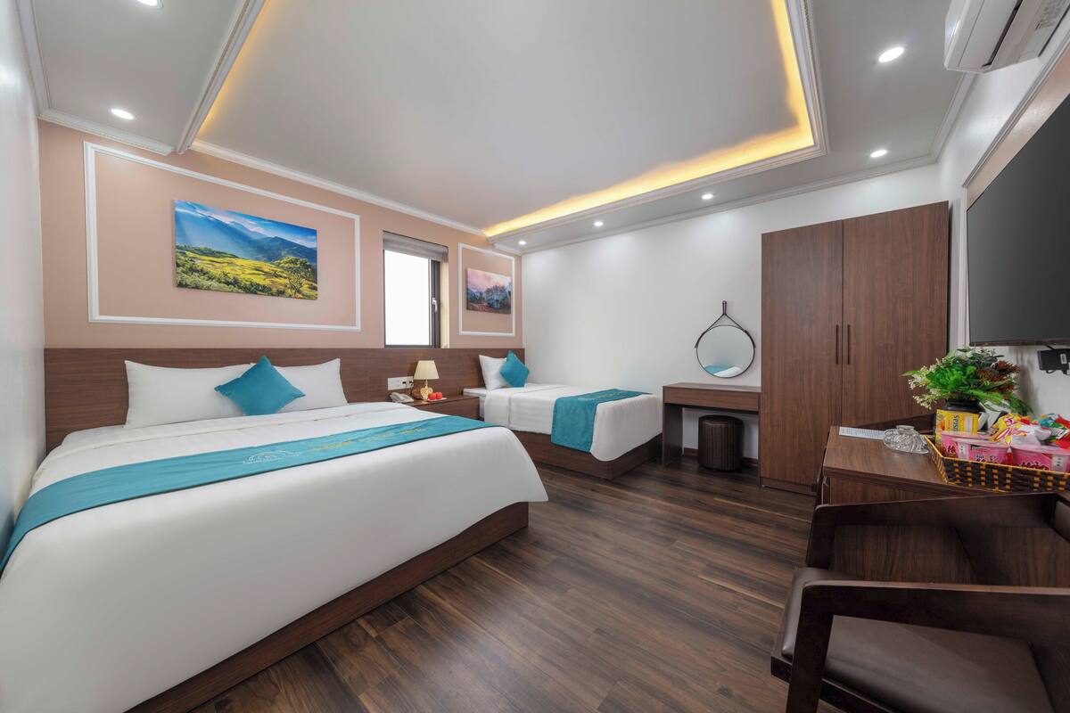 A hotel room with a large bed, a smaller bed, a desk with a mirror, and a TV.