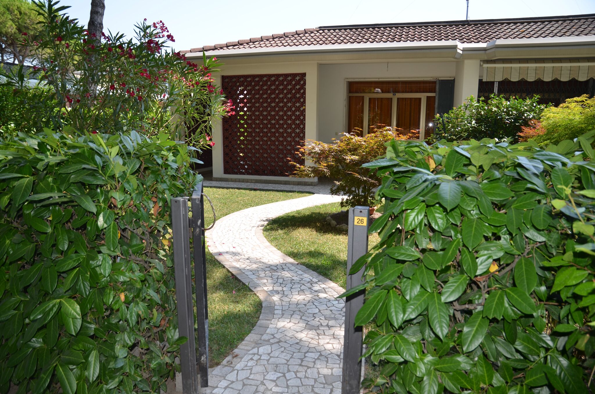 Une maison avec un toit en tuiles, un chemin pavé menant à l’entrée et une plaque portant le numéro 26.