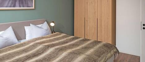 A bedroom with a bed, a wooden wardrobe, a nightstand with a lamp, and a framed picture on the wall.