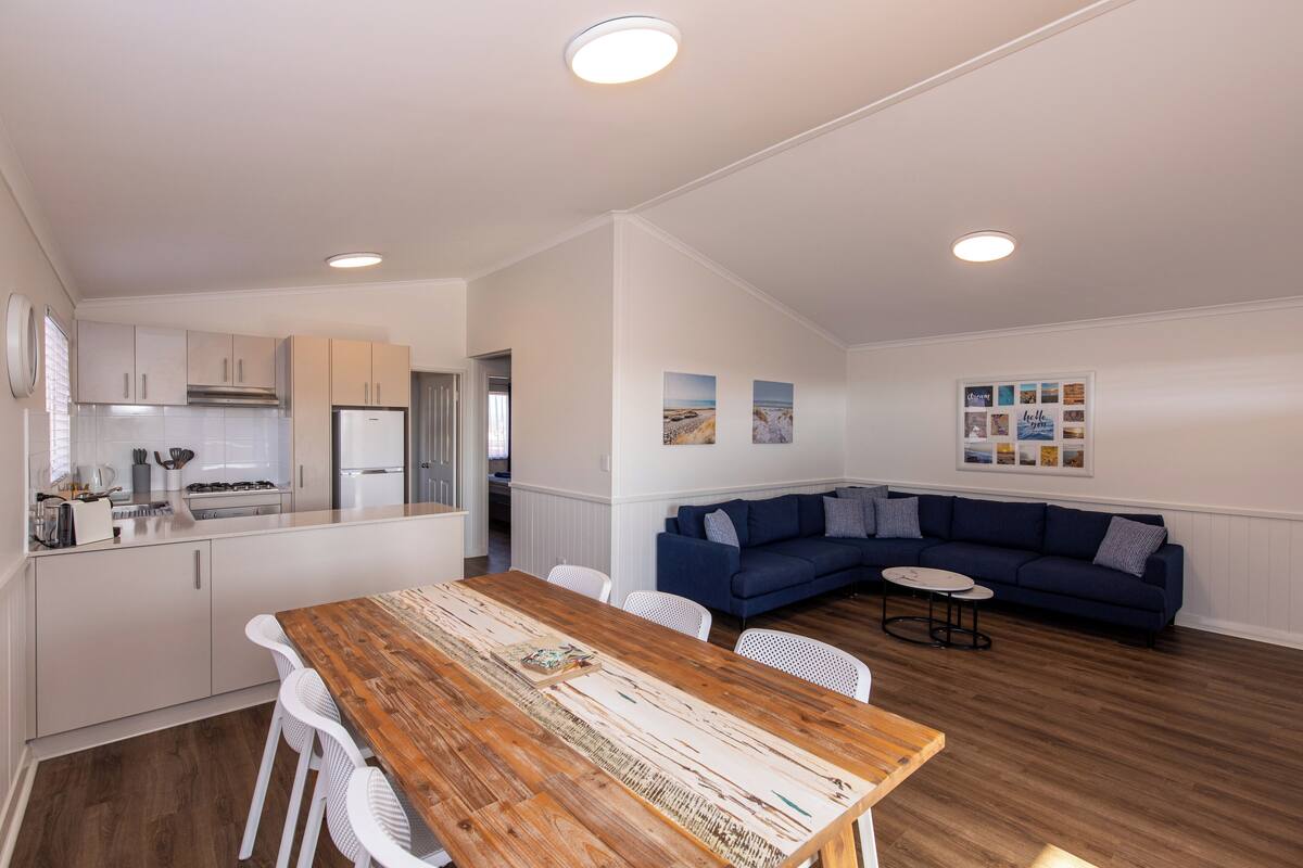 Eine moderne Küche mit weißen Schränken, einem Holzespeisetisch und einem blauen Ecksofa.