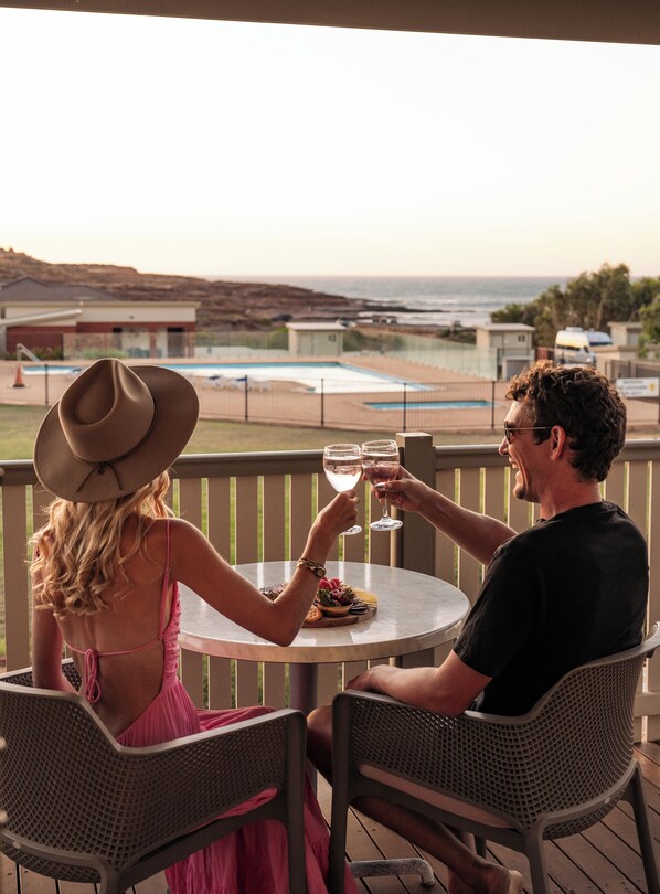 Una pareja sentada a una mesa redonda en una terraza de madera con vistas a una piscina y al océano.
