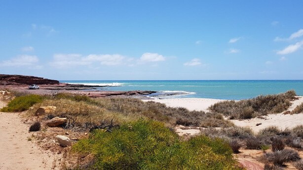 Een kustlandschap met een zandstrand, rotsformaties en schaarse begroeiing.