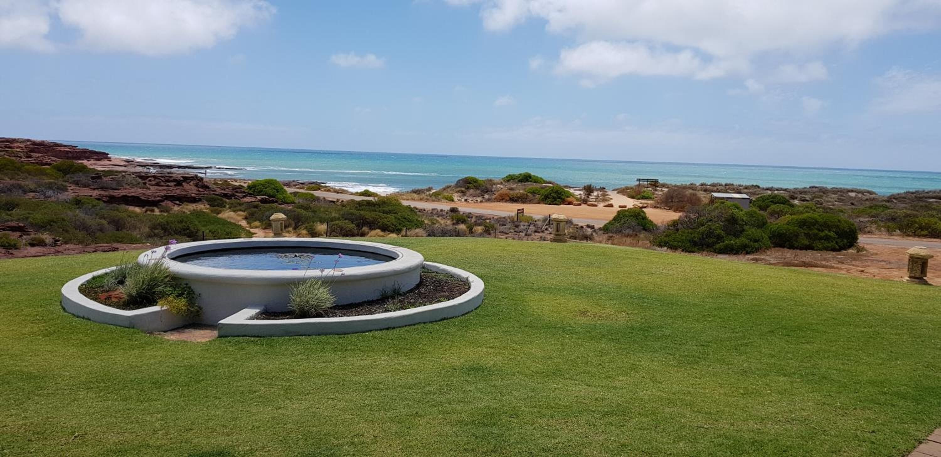 Un bain à remous circulaire installé sur une pelouse, offrant une vue sur l’océan et un paysage rocheux.